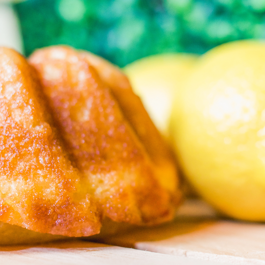 A close up photo of Luxurious Lemon Rum Cake on a wooden table accompanied by a frozen mixed beverage and fresh lemons