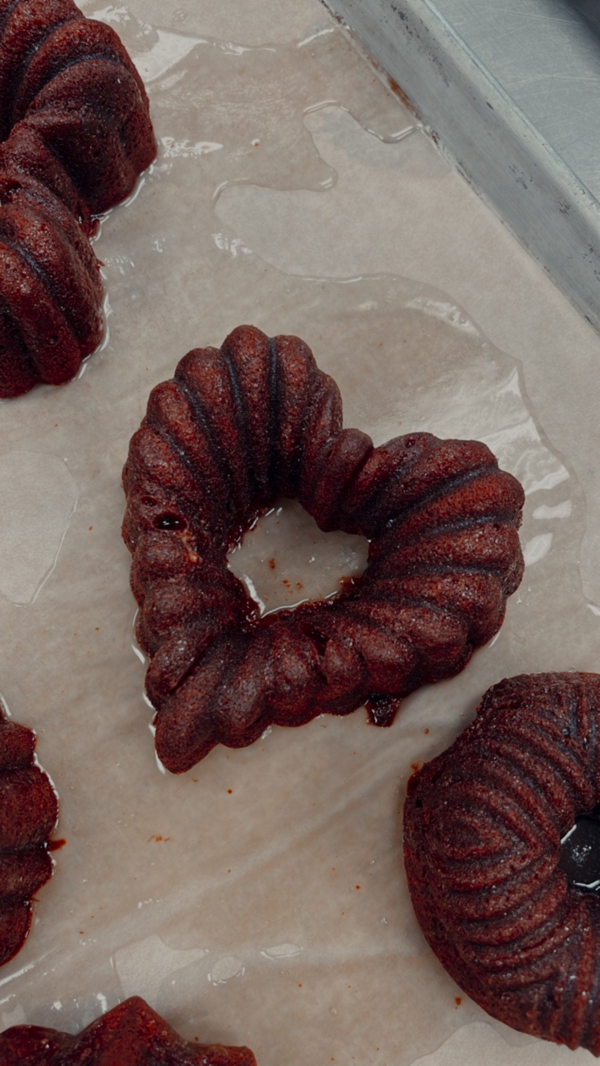 A photo of a red velvet bourbon cake with a heart-shaped cut-out in the center, displayed on a cooling rack.