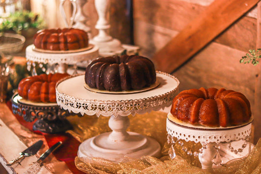 Rum Cake and Whiskey Cake on raised Victorian-style platters on a decorated table against a wooden background. 