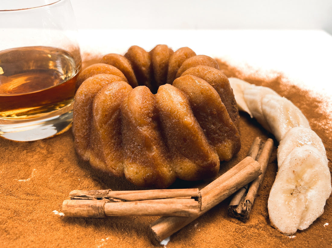 A photo of rum cake with cinnamon, fresh bananas and a glass of whiskey