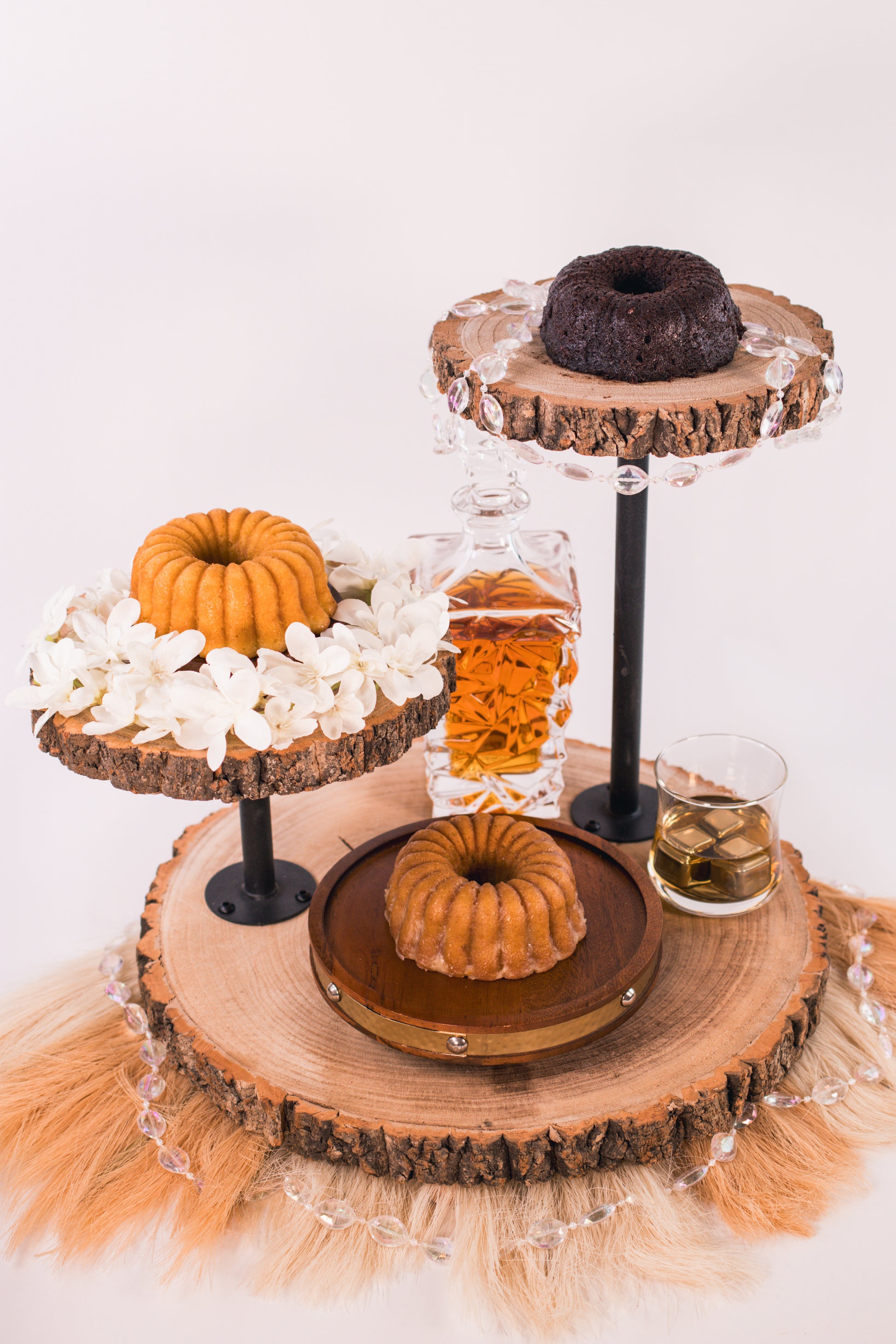Wooden tiered cake stand with chocolate rum cake, vanilla rum cake and cinnamon banana whiskey cake on a white background