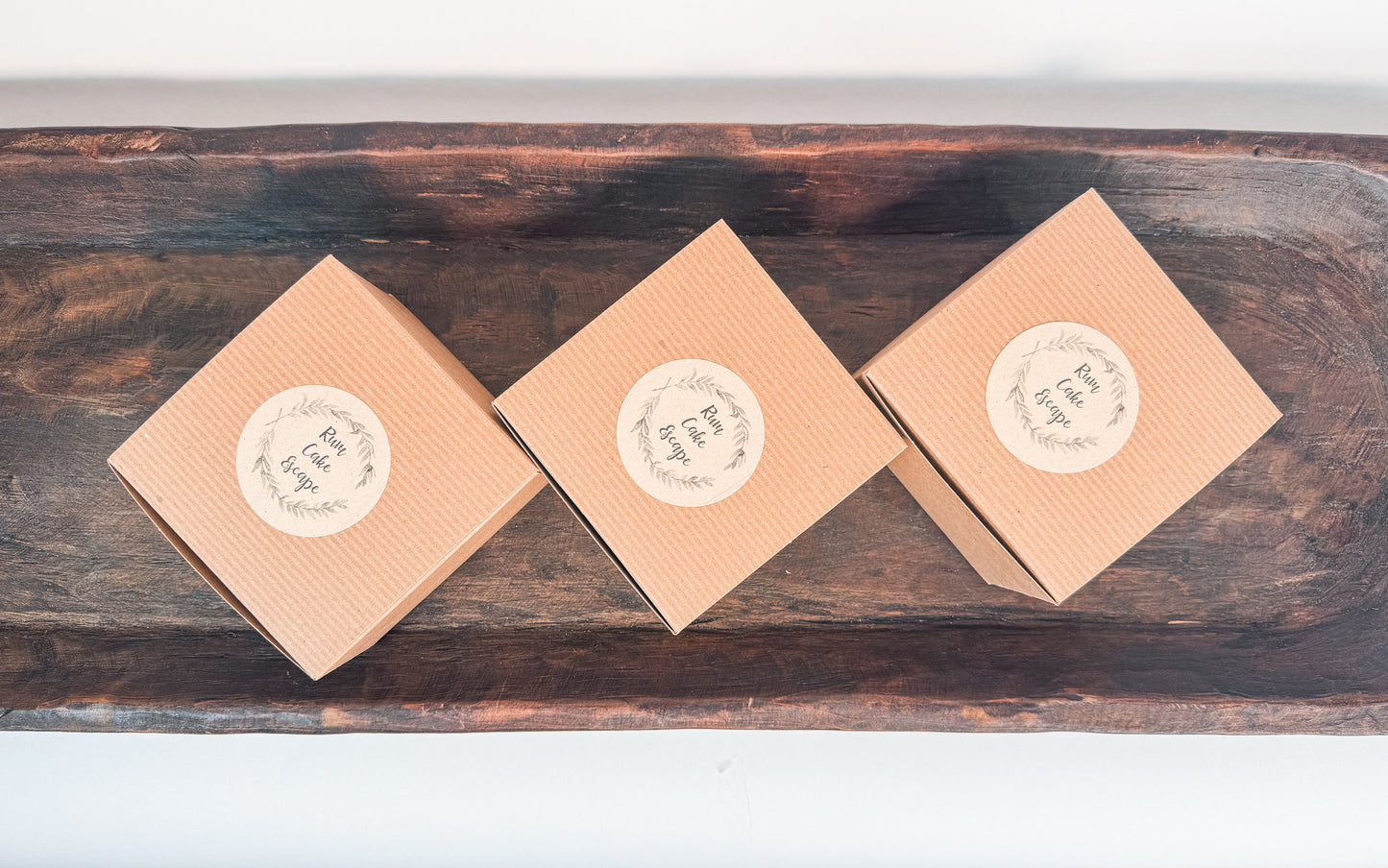 Three brown kraft cake boxes with Rum Cake Escape Logo labels on a wooden surface