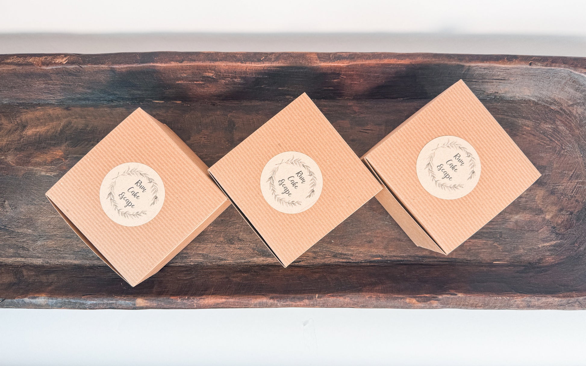 Three brown kraft cake boxes with Rum Cake Escape Logo labels on a wooden surface