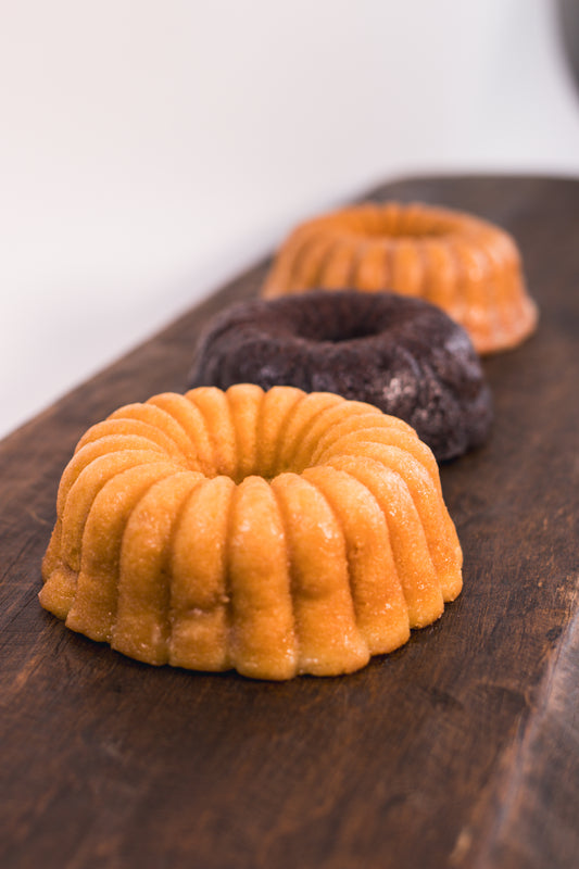 Vanilla rum cake, chocolate rum cake and cinnamon banana whiskey cake on a wooden board with a white background