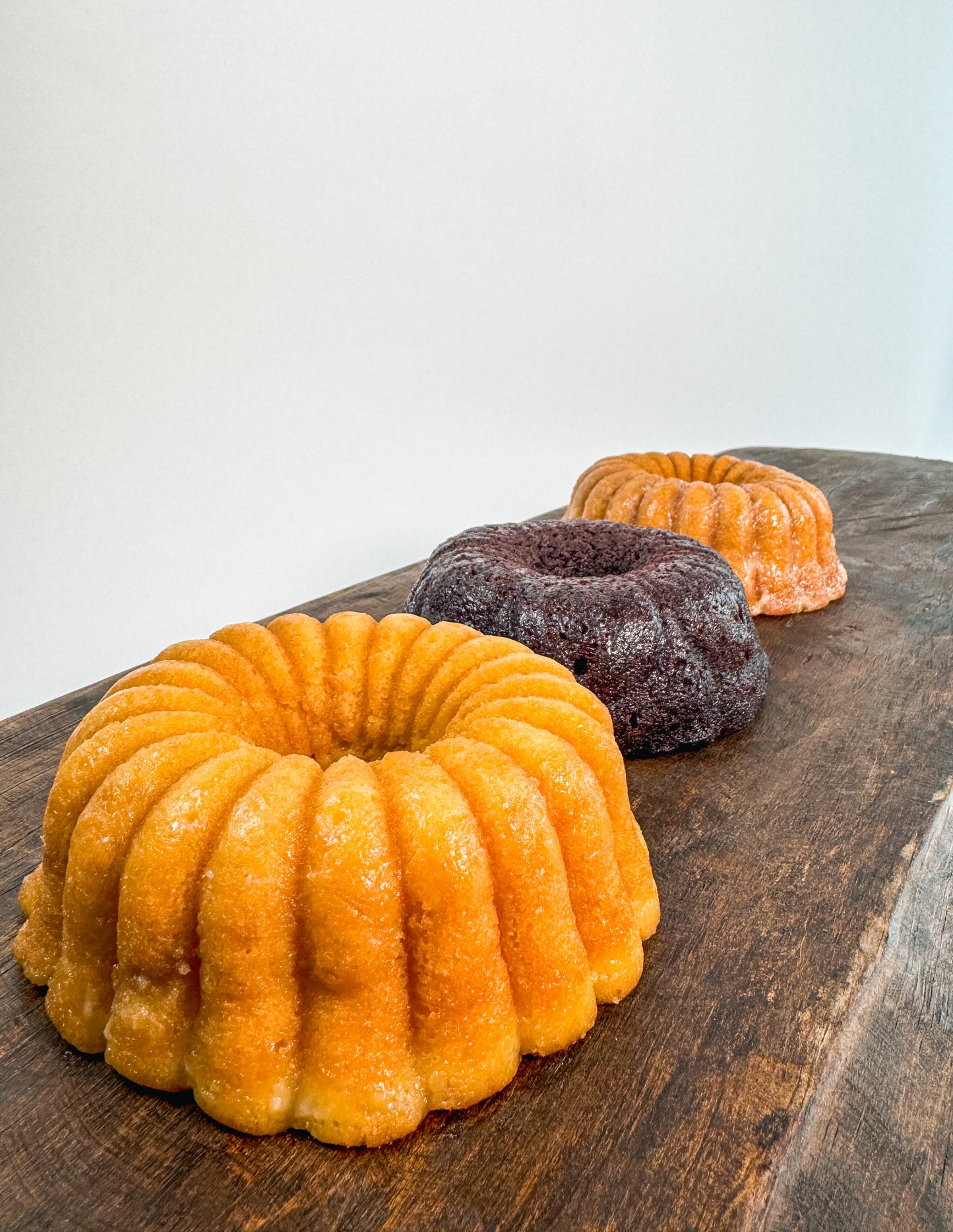 Vanilla rum cake, chocolate rum cake and cinnamon banana whiskey cake on a wooden board with a white background