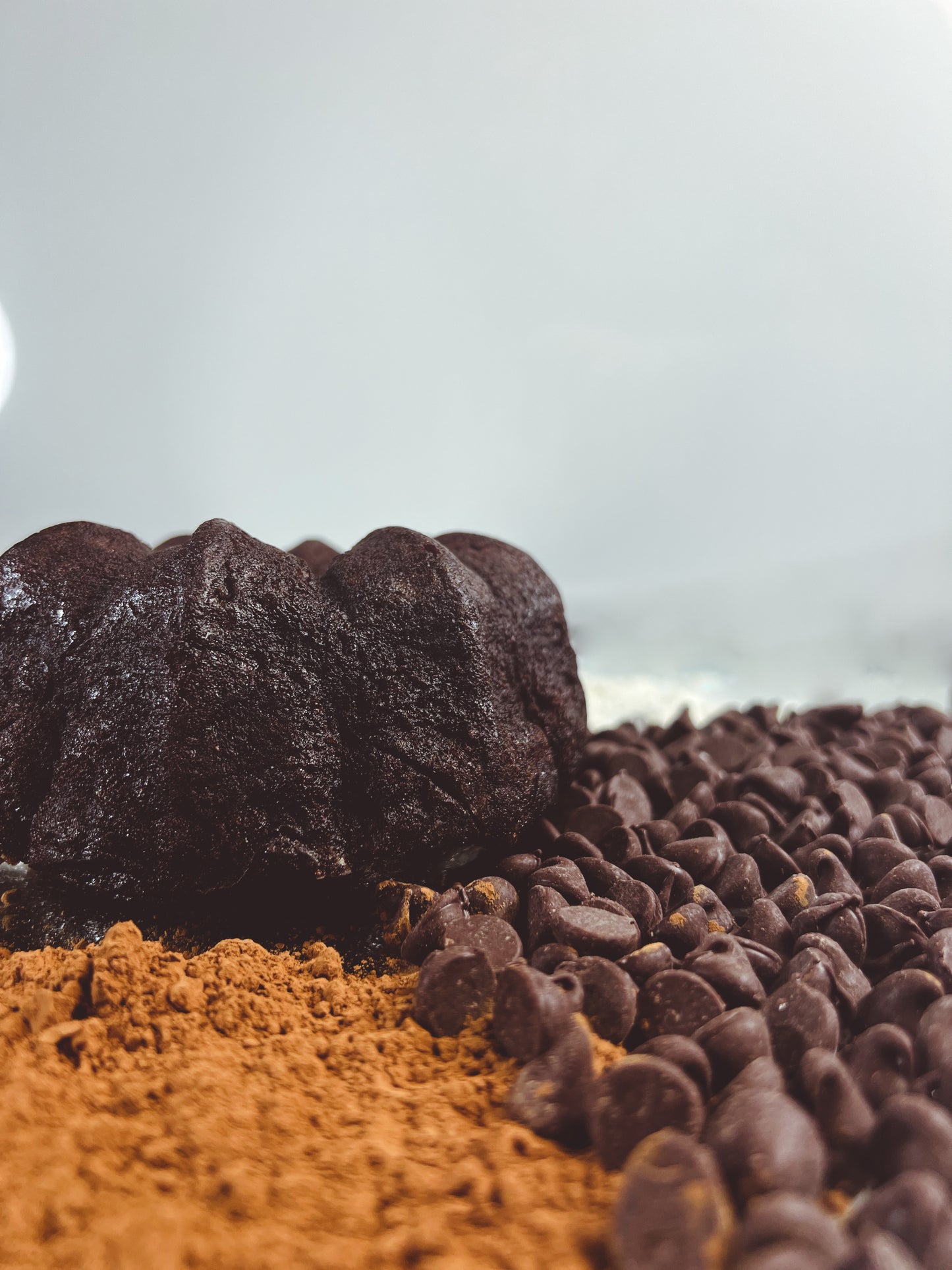 A photo of Blissful Chocolate Rum Cake surrounded by fresh cocoa powder and milk chocolate chips on a white background.