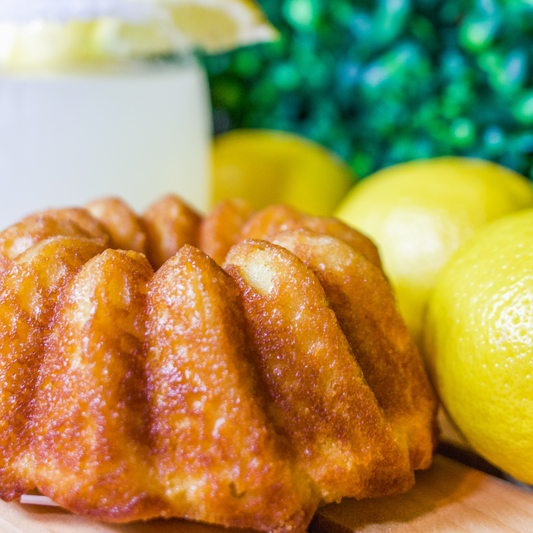 A photo of Luxurious Lemon Rum Cake on a wooden table accompanied by a frozen mixed beverage and fresh lemons