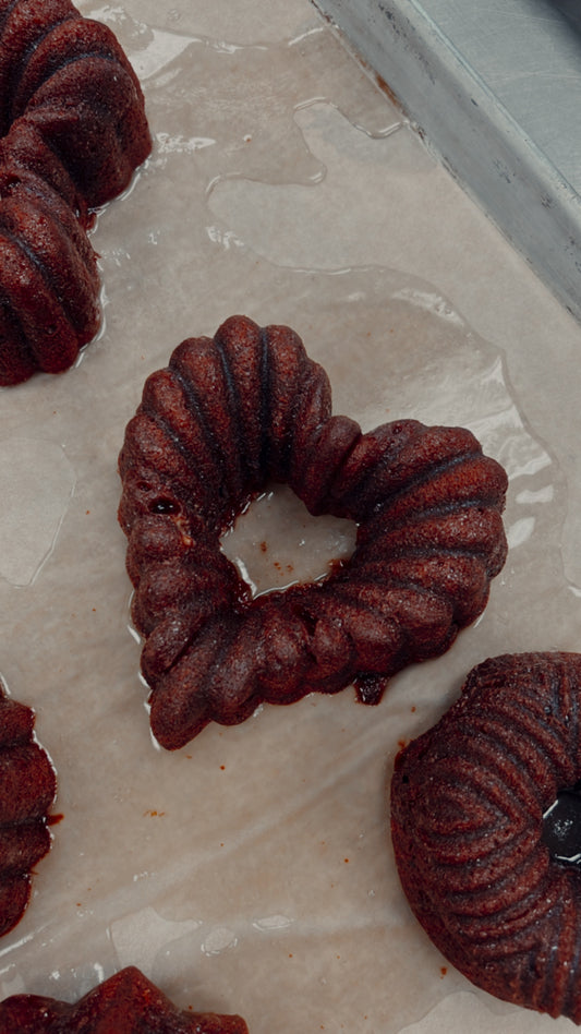 A photo of a red velvet bourbon cake with a heart-shaped cut-out in the center, displayed on a cooling rack.